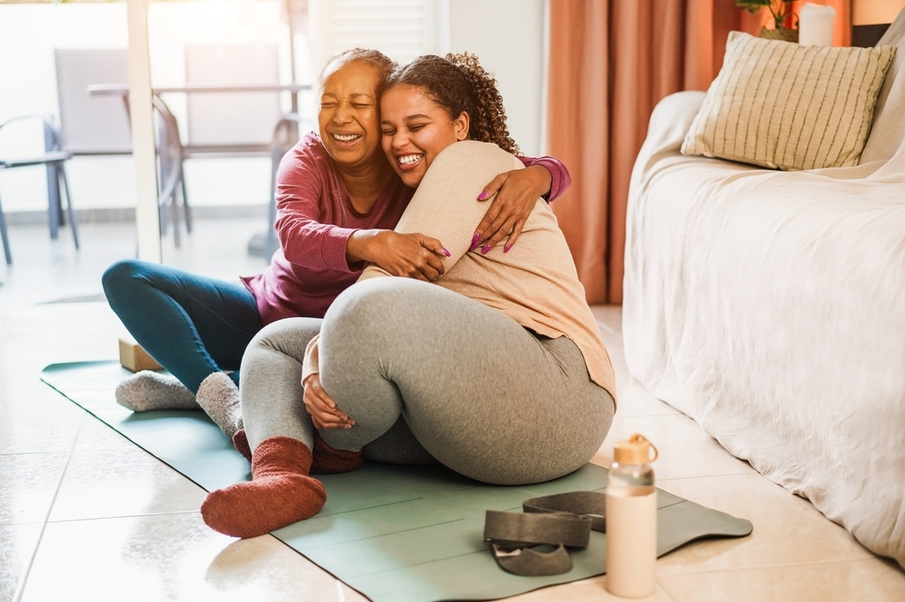 Two Women Sitting On Floor Hugging And Smiling